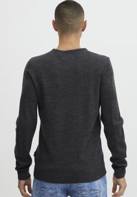 Pull en tricot gris foncé avec un col rond, des manches longues et un ourlet côtelé. Présente un matériau texturé et un minimalisme sur l'étiquette latérale.