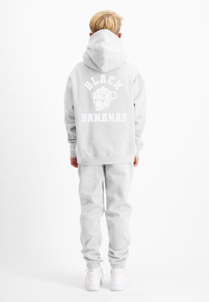Child with blond hair wearing a light gray hoodie and sweatpants, showing a "Black Bananas" logo with a gorilla face on the back of the hoodie.