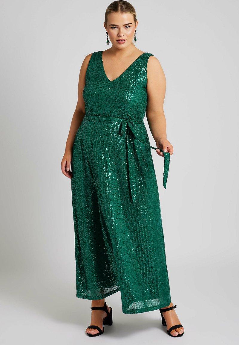 Grön paljettklänning med v-ringning, breda axelband och knytband i midjan. Klänningen som går till golvet har en något utsvängd kjol och en subtil glans.