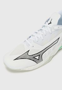 White athletic shoe featuring a mesh upper, black accents with linear patterns, a textured side design, and a light green sole.