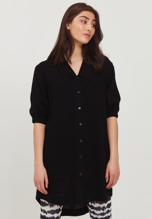 Schwarzes Hemdkleid mit weitem Kragen, kurzen Puffärmeln und einem längeren Rückensaum. Hergestellt aus einem glatten Stoff mit einer leicht durchscheinenden Textur.