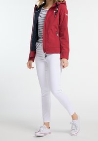 Röd softshell-jacka med huva, zipfickor och marinblå foder. Bärs över en randig skjorta och kombineras med vita slim-fit byxor och sneakers.