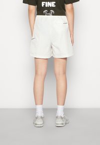 Pantalones cortos blancos con un acabado texturizado, que cuentan con bolsillos traseros y una cinturilla elástica. Combinados con zapatillas grises y calcetines blancos.