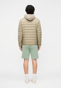 Jachetă bej pufosă cu glugă, cu model matlasat orizontal, purtată peste pantaloni scurți verde mentă și șosete albe până la gleznă, cu pantofi bej.