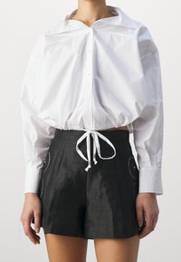 Hvid bomulds skjorte med bred krave og gathered talje; parret med sorte shorts med broderede detaljer og en bindelukning.