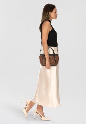 Bolso marrón texturizado con una correa negra, combinado con una blusa sin mangas negra y una falda de satén crema, y zapatos de tacón altos beige.