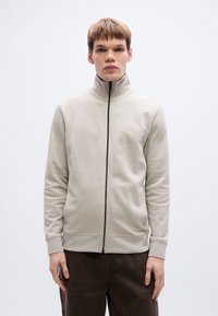 Ανοιχτό γκρι φούτερ με φερμουάρ, ψηλό γιακά, ελαστικές μανσέτες και τελείωμα στη μέση. Διαθέτει μικρό λογότυπο στο στήθος. Ομαλή υφή.