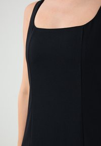 Czarny bezrękawnik z kwadratowym dekoltem, gładki materiał i subtelne pionowe szwy, które nadają dopasowany wygląd. Brak widocznych wzorów lub elementów metalowych.