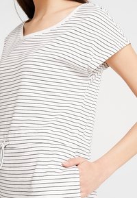 Randig bomullstopp med V-ringning, korta ärmar och dragsnöre vid midjan. Färg: vit med svarta ränder. Inkluderar sidofickor.