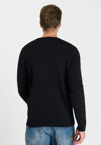 Zwarte trui met een ronde hals en lange mouwen, gemaakt van een gladde stof, met geribbelde manchetten en zoom, gedragen over vervaagde blauwe jeans.