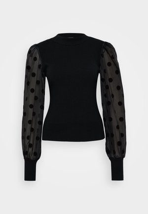 Črna jopica z prilagojenim rebrastim korpusom in prozornimi napihnjenimi rokavi z črnimi pikami. Črni pleteni manšeti dopolnjujeta dizajn.