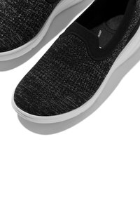 Zwarte instapschoenen met een bovenwerk van gestructureerde stof, elastische rand en contrasterende witte rubberen zool. Heeft een glad en lichtgewicht ontwerp.