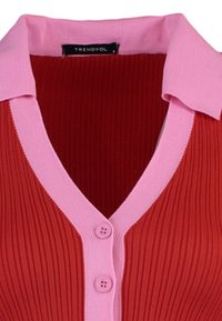 Ärmelloses, geripptes Stricktop in dunklem Rot mit einem hellrosa, flachen Kragen und einer Knopfleiste mit drei runden Knöpfen. Markenetikett sichtbar.