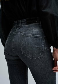 Jeans de denim gris oscuro con una cintura alta, una textura suave y dos bolsillos traseros con una ligera curvatura.