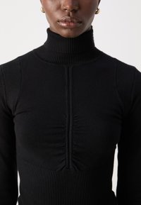 Zwarte geribde turtleneck top met een strakke pasvorm, geplooide voorzijde en gestructureerde contrasterende schouderaccenten.