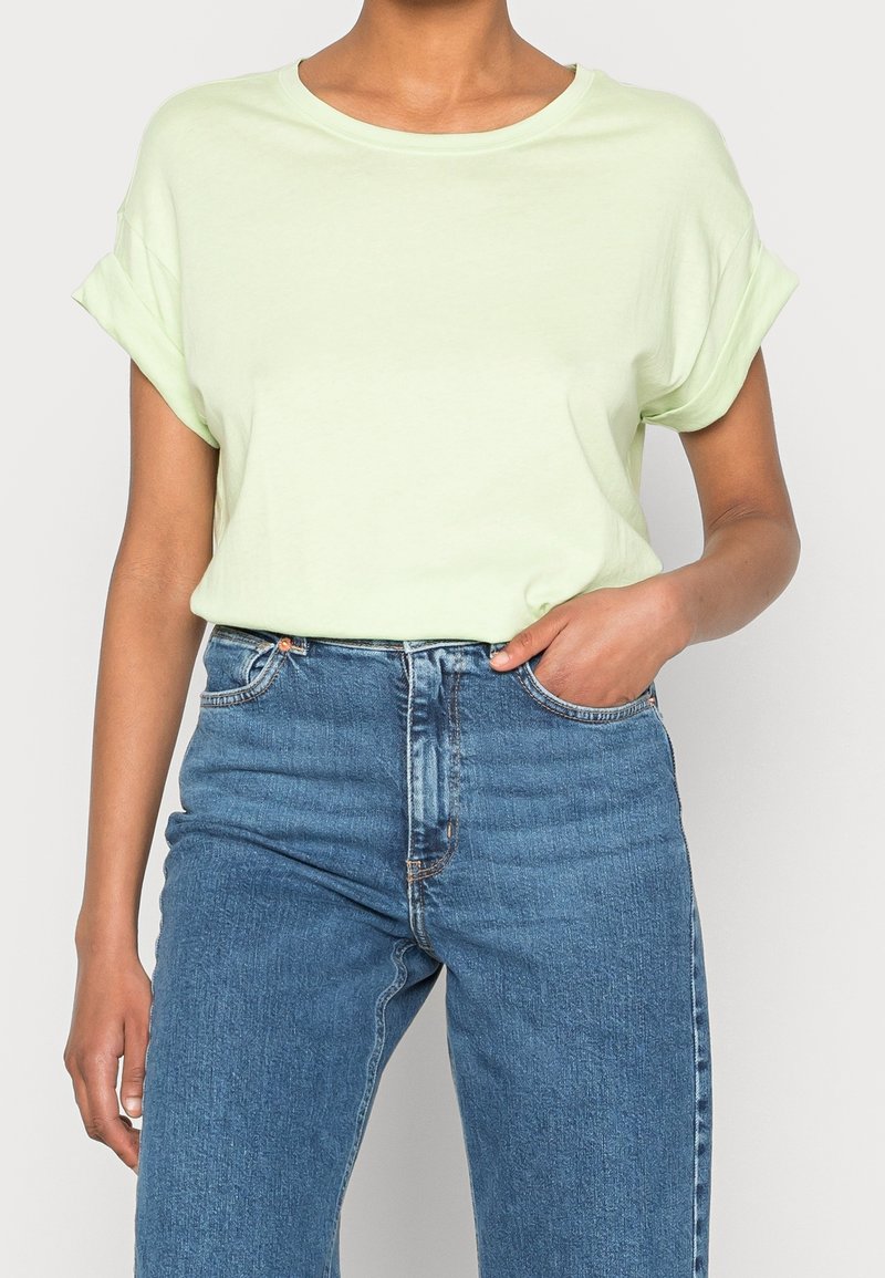 Jasnozielona bawełniana koszulka z podwiniętymi rękawami, zestawiona z wysokimi, niebieskimi dżinsami z guzikiem i przednimi kieszeniami.