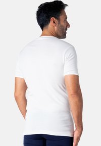 T-shirt blanc à manches courtes en coton, design ajusté avec un col rond, texture lisse et sans logos ni motifs visibles.