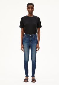 Schwarzes T-Shirt mit kurzen Ärmeln, kombiniert mit hochgeschnittenen, dunkelblauen Skinny-Jeans und schwarzen Slippers. Einfaches, figurbetontes Design mit moderatem Stretch.