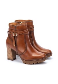 Botas de tobillo de cuero marrón con punta redondeada, cremallera lateral, detalle de hebilla y tacón de madera apilada. Suela texturizada para mayor agarre.