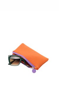Pomarańczowe etui na okulary wykonane z tkaniny z fioletowym zamkiem błyskawicznym, trzymające zielone okulary przeciwsłoneczne z wyraźnymi kwadratowymi oprawkami i brązowymi soczewkami.