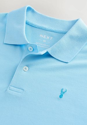 Polo bleu clair en coupe régulière, avec une texture douce, deux boutons et un petit motif brodé sur la poitrine.