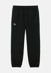 Crne sportske hlače s zelenom bočnom prugom, elastičnim pojasom i manžetnama. Na prednjem dijelu nalazi se mali Lacosteov logo krokodila.