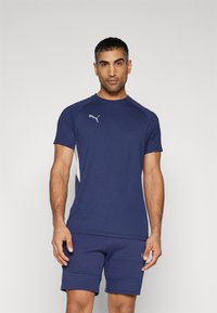 Marineblå kortærmet atletisk skjorte med hvide sidepaneler og Puma-logo. Suppleret af matchende marineblå shorts. Glat tekstur.