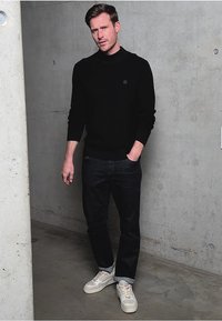 Pull noir à col rond, jean foncé et baskets blanches. Texture lisse, coupe décontractée et design minimaliste sans motifs.