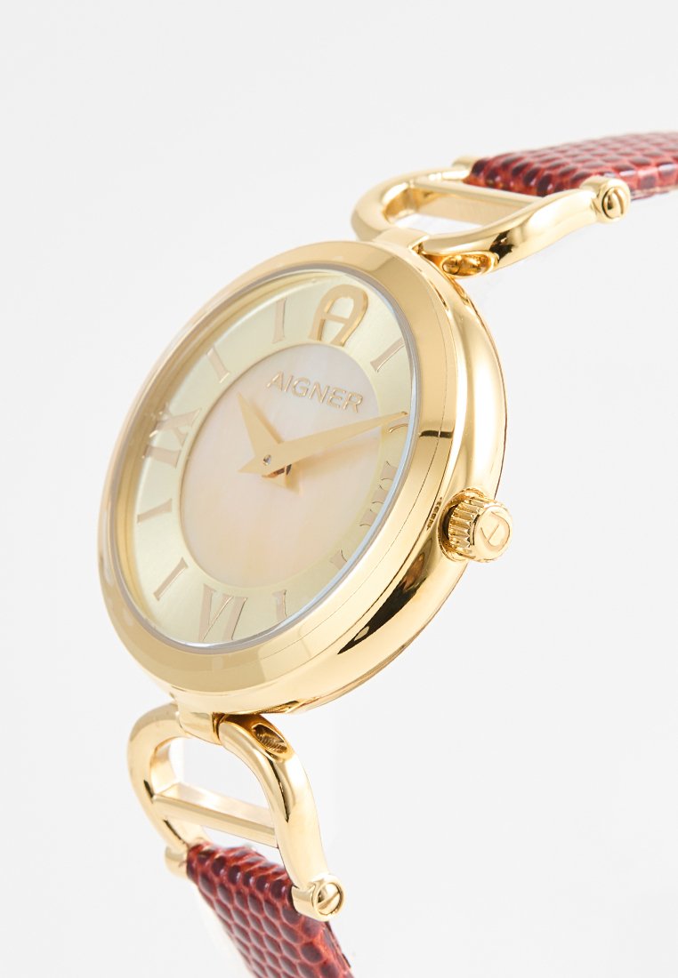 Montre dorée avec un cadran en nacre, des chiffres romains et un bracelet en cuir texturé marron rougeâtre. Caractérisée par un boîtier rond et une couronne.