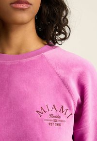 Rosa kordflanelltröja med ribbad halsringning. Har broderad text "MIAMI Florida USA EST 1988" i brunt på vänster framsida.
