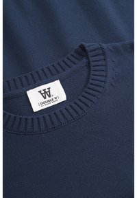 Tumed sinine sviiter ribaga ümara kaelusega, sile tekstuur ja silmatorkav silt "DOUBLE W" kaubamärgilt Wood Wood. Lihtne ja klassikaline disain.