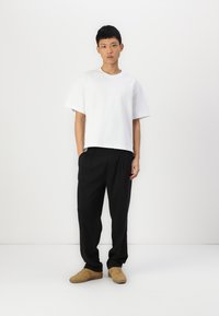 Maglietta bianca a maniche corte abbinata a pantaloni neri a vestibilità ampia e sneakers beige; tessuto morbido con una silhouette rilassata.