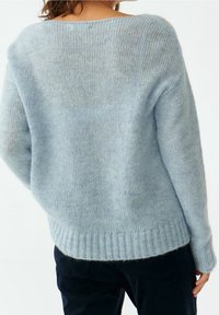 Jasnoniebieski, dzianinowy sweter o luźnym kroju, szerokim dekolcie, prążkowanym wykończeniu i miękkiej fakturze, wyeksponowany z tyłu.