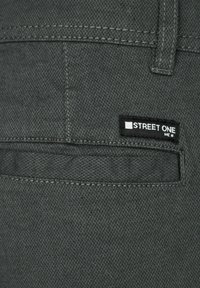 Mörkgrå byxor i texturerat tyg, med en bakficka som har en liten svart etikett med texten "STREET ONE."