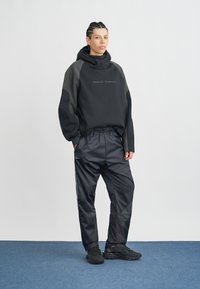 Mustmust mustraamat musta kapuutsiga, millel on tekstuuriga õlad, koos mustade läikivate treeningpükstega, millel on külgedel triibud ja vöökoht. Mustad tossud.