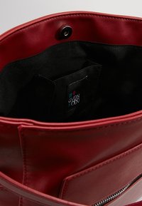 Sac à main en cuir rouge avec une texture lisse, doté d'un intérieur noir, d'une fermeture par pression et d'une poche extérieure zippée. Comprend une étiquette de marque visible à l'intérieur.