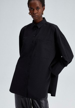 Black button-up shirt with a relaxed fit, featuring a point collar, long sleeves, and a front pocket. Made of soft, textured fabric.