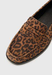 Brown suede loafers featuring a leopard print pattern, a rounded toe, and stitched detailing. Black rubber sole with minimal texture.