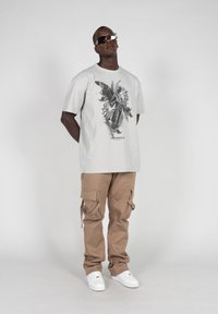 Light gray cotton t-shirt featuring a black graphic design; paired with tan cargo pants, showcasing multiple pockets and a relaxed fit.
