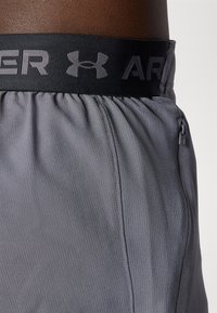Sivé športové šortky s čiernym elastickým pásom a bielym logom "Under Armour". Hladká, ľahká tkanina s textúrovanými detailmi.