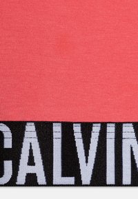 Koralna tkanina z gladko teksturo, ki ima kontrastni črni pas z belim napisom "CALVIN". Preprost, moderen dizajn.