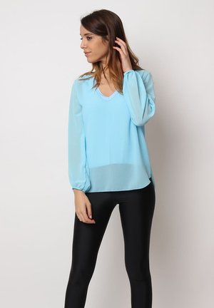 Blusa de manga larga azul claro con escote en V, puños fruncidos y un corte holgado, combinada con leggings negros. Tejido suave y ligero.
