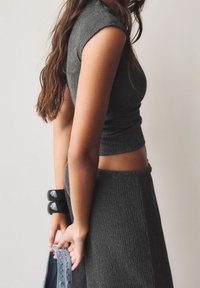 Crop top en tricot côtelé gris avec des manches courtes, associé à une jupe taille haute assortie. La personne tient un sac bleu avec des clous et porte des bracelets noirs.