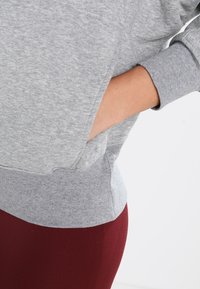 Gray sweatshirt with long sleeves, ribbed cuffs, and side pockets. Soft texture and relaxed fit. Paired with burgundy leggings.