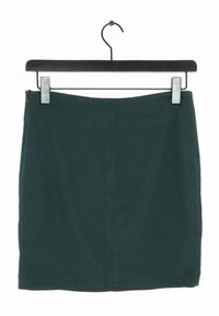 Falda de algodón verde colgada en una percha negra, con un diseño simple y recto, con una cremallera oculta en la parte trasera y sin patrones visibles.
