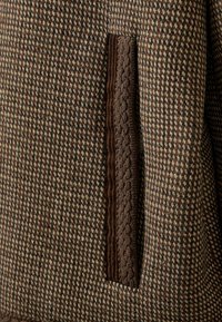 Gros plan d'un tissu pied-de-poule marron et beige avec un détail de bordure verticale texturée marron foncé.
