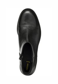Chaussure en cuir noir avec une texture lisse, insert latéral élastique, bout rond et profil élancé. Présente une fermeture éclair discrète sur le côté.