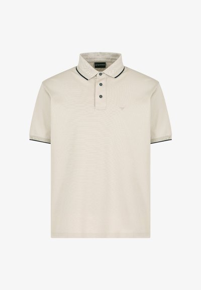 Polo de color beige claro con una superficie texturizada, tapeta de dos botones, cuello y acentos de manga en contraste oscuros, y logotipo bordado en el lado izquierdo del pecho.