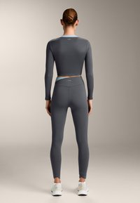 Top sportivo corto grigio a maniche lunghe abbinato a leggings grigi a vita alta, con un dettaglio azzurro chiaro in vita.