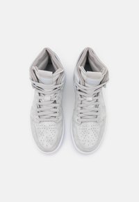 Zapatillas altas en ante gris claro con puntera perforada, cordones planos y cuello acolchado en el tobillo. Suela de goma blanca, con branding mínimo.
